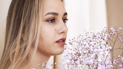 Girl's face with clean smooth skin, naked makeup on the background of gypsophila branches in the studio. Model