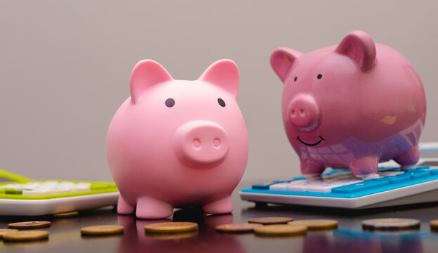 Dois cofrinhos sobre uma mesa com moedas e calculadoras. Conceitos de finan&ccedil;as e economia.