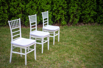 Rows of empty white luxury chairs sitting on a green lawn before a wedding ceremony in summer.