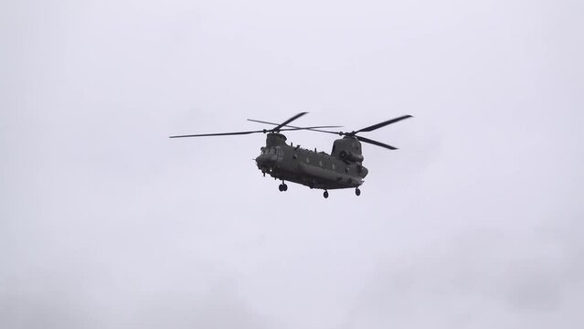 close up of an RAF Chinook tandem-rotor CH-47 helicopter flying fast and low in a cloudy blue grey sky on a military battle exercise, Wilts UK