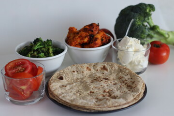 A serving of whole wheat Indian flat bread along with air fried grilled chicken, sauteed broccoli and fresh tomato slices