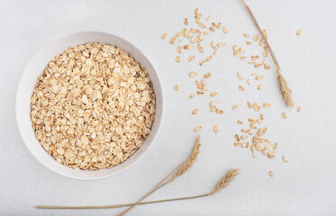 A bowl of oat flakes and ears of wheat on a light background 