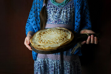 Holiday Shrovetide Shrovetide. Handmade Russian pancakes in the hands of a young girl. National Russian Festival. The girl is dressed in the Russian style, with a pancake during Maslenitsa. Spring is 