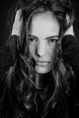 Black and white portrait of a beautiful young desperate woman with her head in her hands and looking at the camera