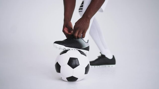 soccer player is tightening shoelace of football boots standing leg on ball, details in photostudio