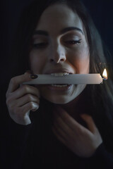 Playing with fire - young beautiful woman with long hair holding a burning candle in her mouth and burning her hair