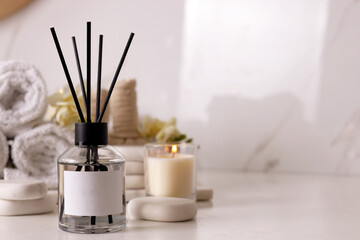 Aromatic reed air freshener and spa stones on white table, space for text