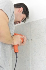 man drills with an electric drill into the wall of tiles in the bathroom
