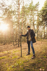 Mystic gamekeeper standing with magic stick on the green moss in the pine forest in the sunlight.