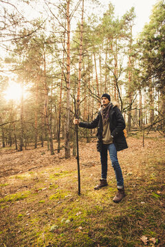 Mystic gamekeeper standing with magic stick on the green moss in the pine forest in the sunlight.