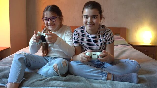 Two little sisters sitting at home on pleasant evening and playing games on a console. They challenge each other to win.