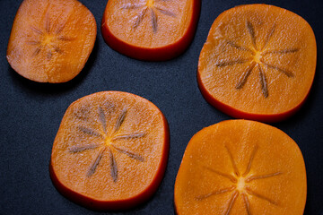 Ripe orange persimmon fruit on black wooden table. Persimmon fruits, cut in half, top view