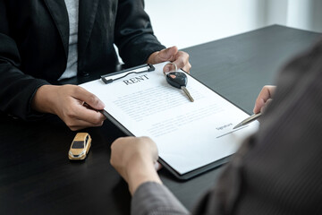 Asian salesman holding rental contract and hand over car key to client while he is holding pen to signing