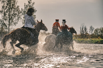 People in old fashion costumes ride on horseback on water and field background. Water drops