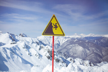 Sign on background of mountains. Sign warning of danger of falling. Triangle on stick. Symbol on yellow background. Carefully abrupt break.
