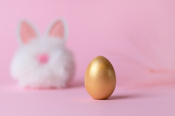 Closeup of a golden easter egg and a toy hare on a pink background, happy easter concept.