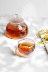 A glass mug or cup with herbal tea and a teapot in sunny day. Spring, summer.