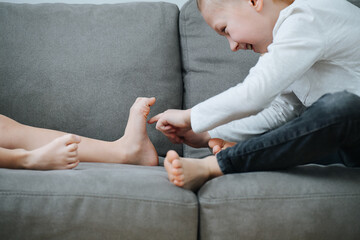 Naughty little boy sneakily tikling his sister's feet.