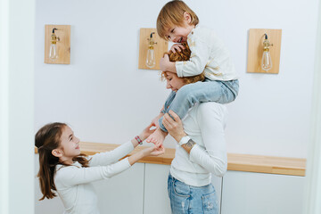 Sister ticklig little boy's feet, while he is sitting on his mother's shoulders - obrazy, fototapety, plakaty