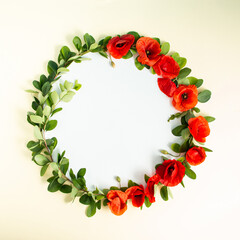 Round frame wreath with red poppies bloom and branches on sandy background. Minimal floral composition. Flat lay. Copy space.