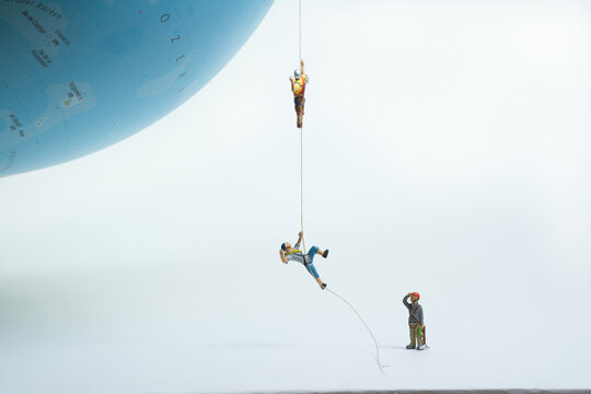 climbers pull themselves up on a rope to a globe