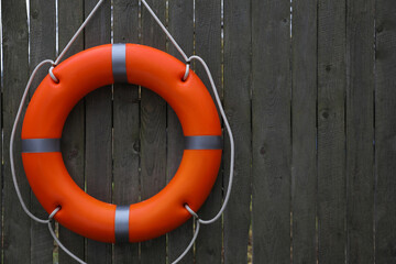 Orange lifebuoy hanging on grey wooden fence, space for text. Rescue equipment