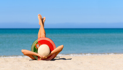 A slender tanned girl on the beach in a straw hat in the colors of the flag of Portugal. The...