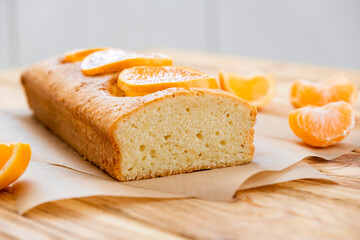Loaf of delicious tangerine pound cake on parchment with pieces of mandarin on rustic wooden background. Slice of citrus pie by classic recipe. Homemade bakery, vegan dessert.