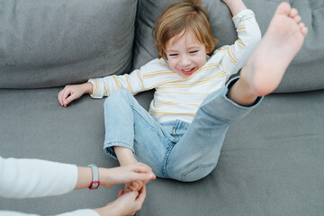 Squirming laughing boy being foot-tickled on the couch. - obrazy, fototapety, plakaty