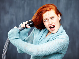 Not the best way to clean your hair. A young redhead with her hair caught in the vacuum cleaner.