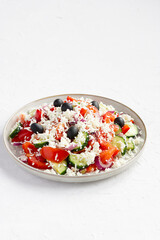 Balkan salad on white concrete background, isolated, vertical plane. Another name of salad is 'Shopska salata'. Recipe: chop cucumber, tomato, pepper, onion, add olive oil and 'sirene' cheese.