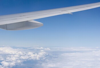 View of above clouds and wing of airplane from window with blue sky background. Use for wallpaper or backdrop.