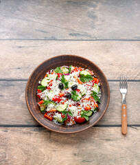 Bowl of Balkan salad. also called 'Shopiski' is on wooden background with fork. Rustic style. Vertical plane. Top view