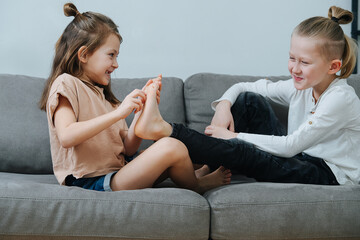 Mischievous girl trying to tickle boy's foot, they both laugh. - obrazy, fototapety, plakaty