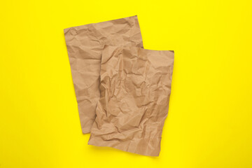 Sheets of crumpled brown paper on yellow background, top view