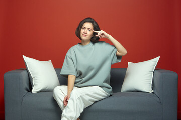Young girl showing stupid gesture with forefinger near temple, sitting on couch. Are you crazy....