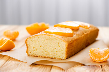 Loaf of gluten free tangerine cake with pieces of mandarin on rustic wooden background. Slice of citrus pie by classic recipe. Healthy nutrition, homemade vegan dessert.