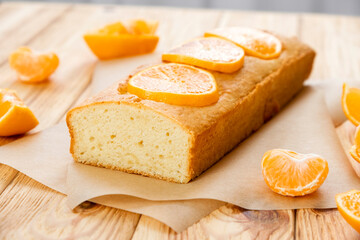 Moist mandarin pound cake on parchment with pieces of fresh tangerine on rustic wooden background. Delicious breakfast, traditional English tea time. Reciepe of citrus pie.