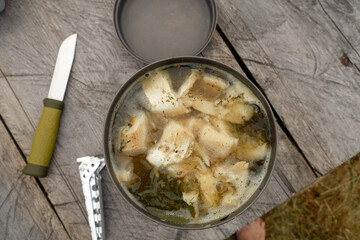 Fish soup in a metal plate on a wooden background. Cooking food on a tourist burner. Traditional...