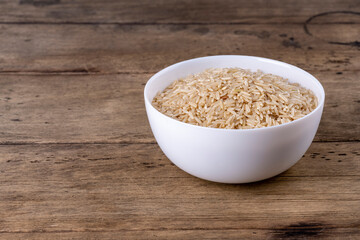 Brown raw Rice Groats In White Bowl Isolated On wooden Background