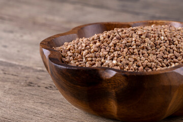 Raw brown buckwheat in a plate on a wooden background.