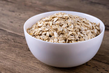 Dry rolled oatmeal in bowl on wooden background