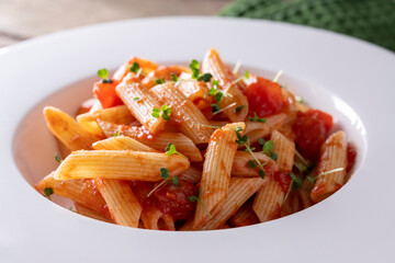 Pasta with tomato in red sauce on a white plate on wooden background.