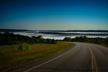 Highway winding into the mist-filled valley under a moonlit night sky