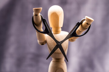 Closeup shot of a small wooden human mannequin holding scissors against a gray background