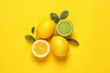 Fresh ripe lemons, lime and green leaves on yellow background, flat lay