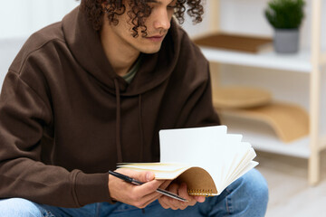 A young man writes in a notebook sitting on a chair in the room Lifestyle