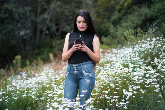 Joven atractiva sonriente  parado sosteniendo un celular en las manos, tel&eacute;fono celular, naturaleza,
