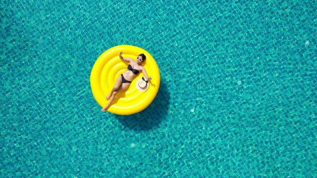 Beautiful young asian woman with yellow inflatable ring relaxing in swimming pool. top view