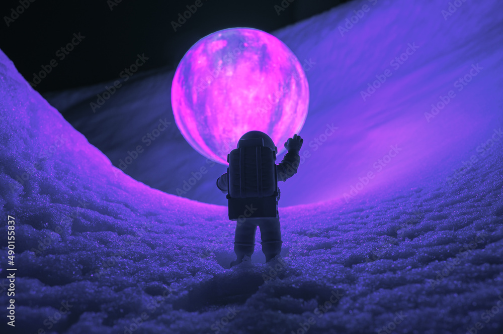 Wall mural silhouette of the toy of astronaut against levitating glowing sphere over surface icy planet covered